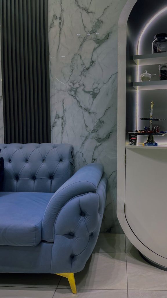 Fabrication meuble Koléa Stylish living room with a blue tufted sofa and modern marble wall backdrop.
